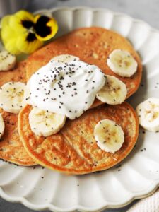 3 low carb protein pancakes on a plate topped with Greek yogurt and sliced bananas.