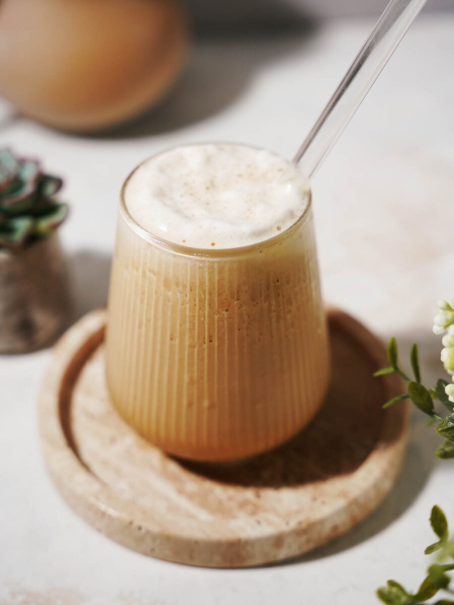 A glass of protein coffee with a straw sitting on a plate.