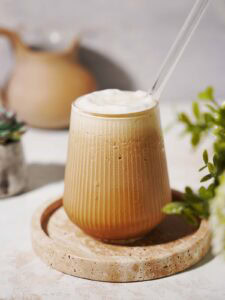 A glass of protein coffee with a straw sitting on a plate.